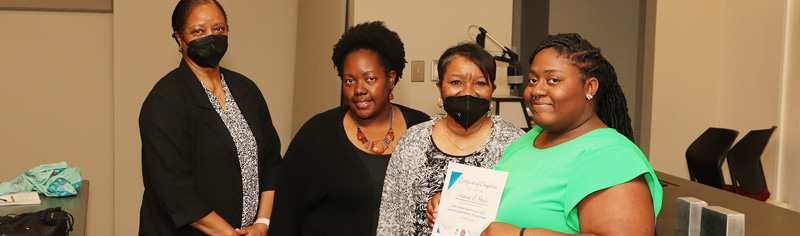 Four black female apprentices holding a certificate of completion